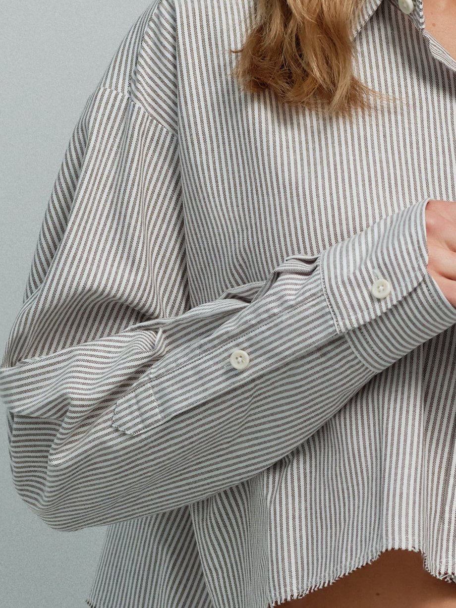 Close-up of brown striped raw-edge oxford shirt showing sleeve cuff and raw hem.