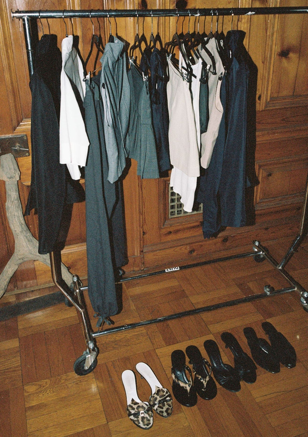 Clothing rack with clothes and shoes on a wooden floor.