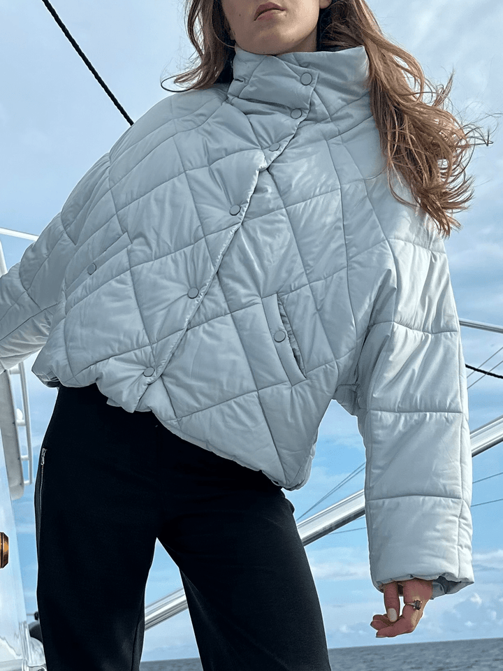 Model wearing a light blue puffer jacket with a high collar, paired with black pants, standing on a boat.