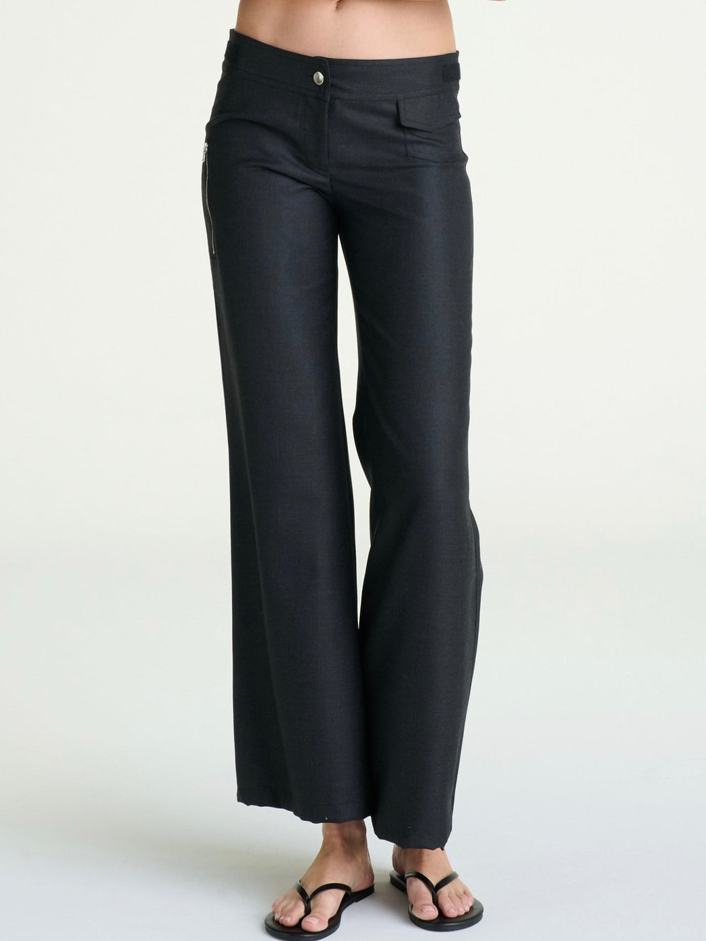 model wearing charcoal wool pants that are tight at the hip and thigh and become wide-leg by the ankles