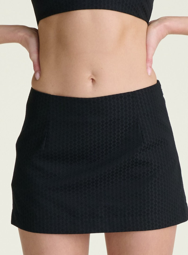 Person wearing a black textured skirt on a plain background