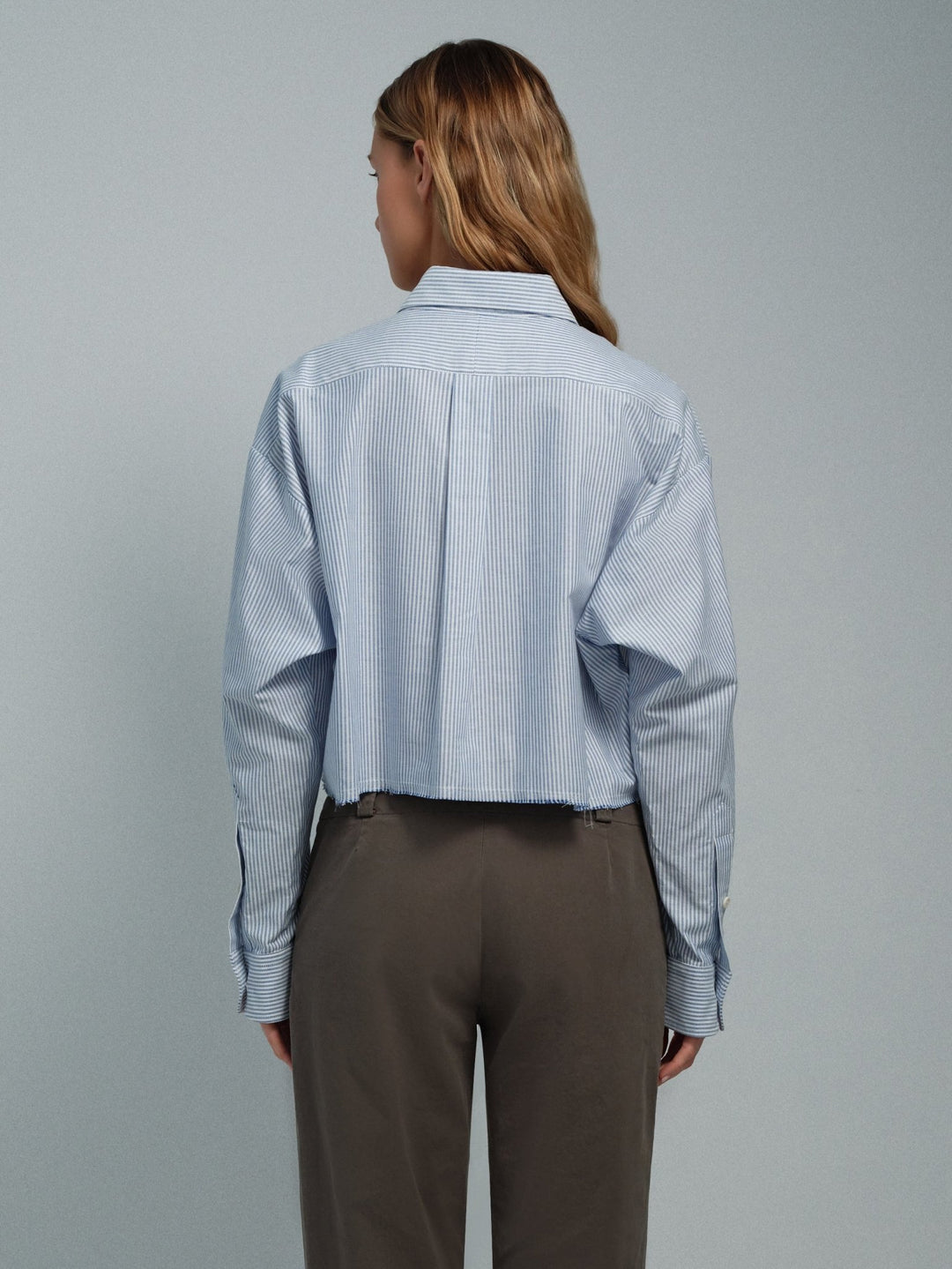 Women’s blue stripe raw-edge oxford shirt, back view showing raw hem and long sleeves.