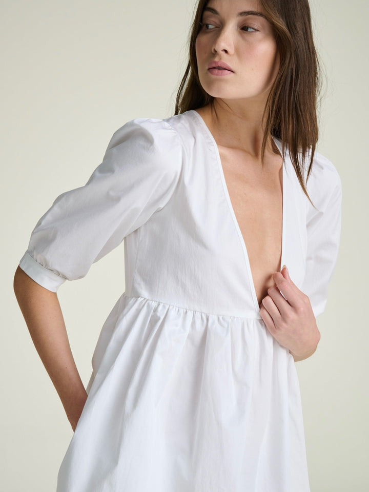 model wearing white dress with puff sleeves and deep v neckline
