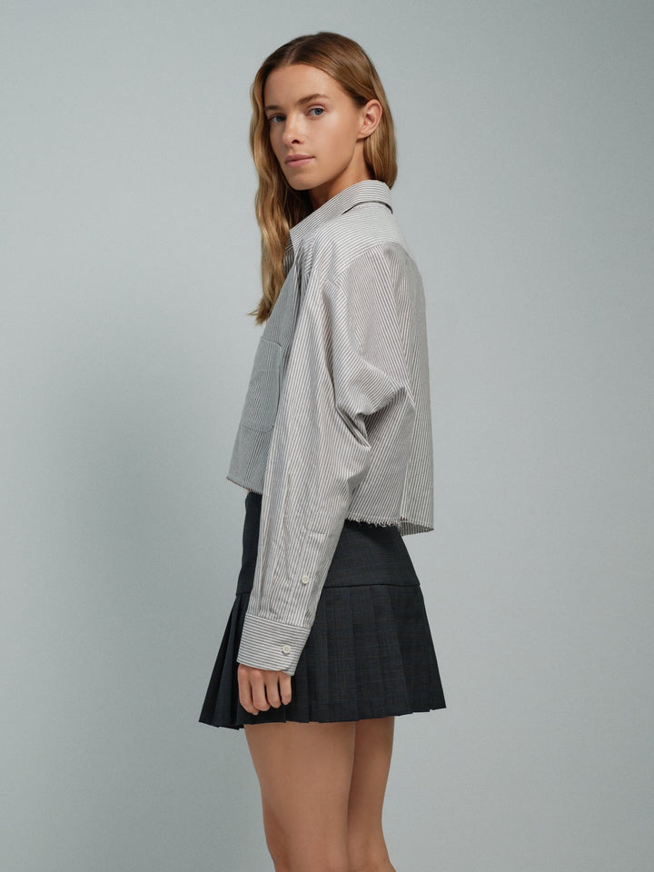 Side on-model view of brown striped raw-edge oxford shirt with cropped hem.