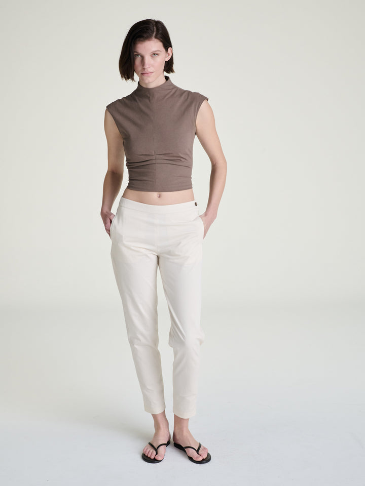 Person wearing a brown top and white pants on a plain background