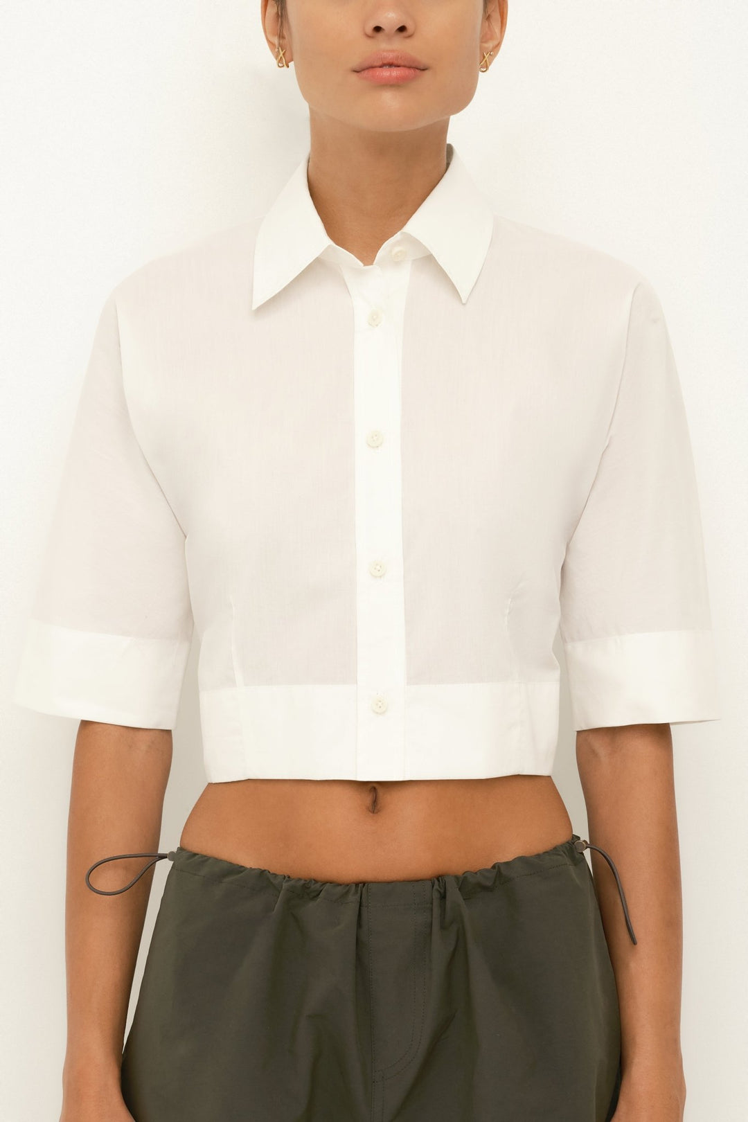 Model wearing a white cropped shirt and green pants on a plain background