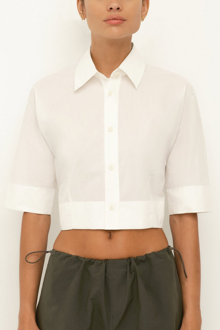 Model wearing a white cropped shirt and green pants on a plain background