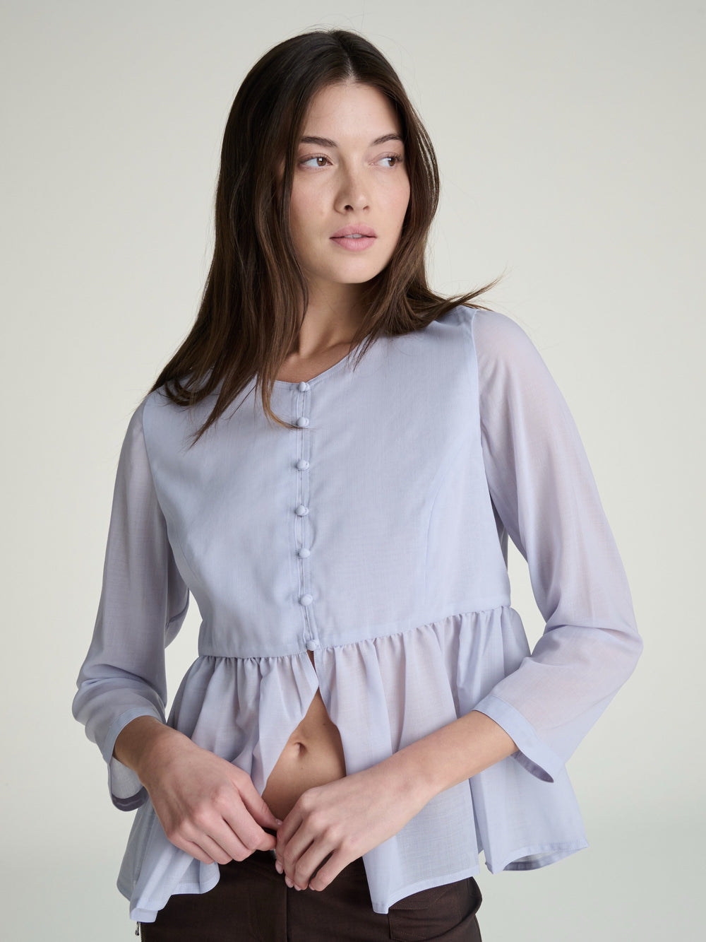 Woman wearing a light blue wool blouse with long sleeves on a gray background