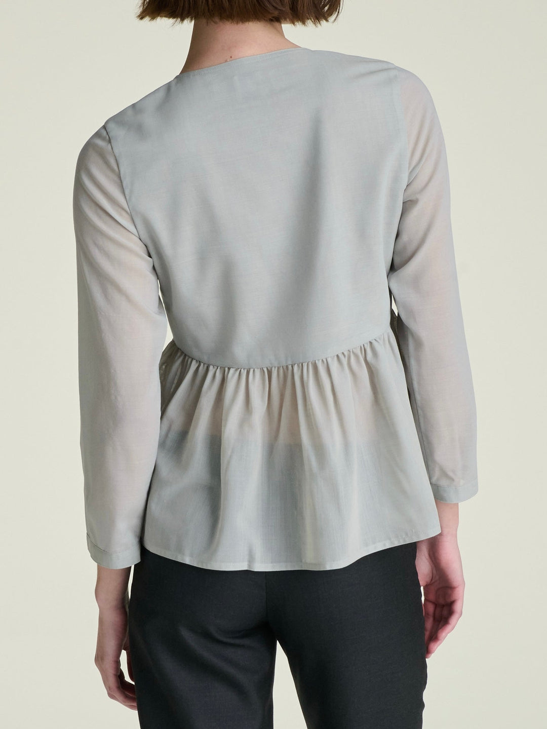 model wearing a lightweight light grey blouse, shown from the back