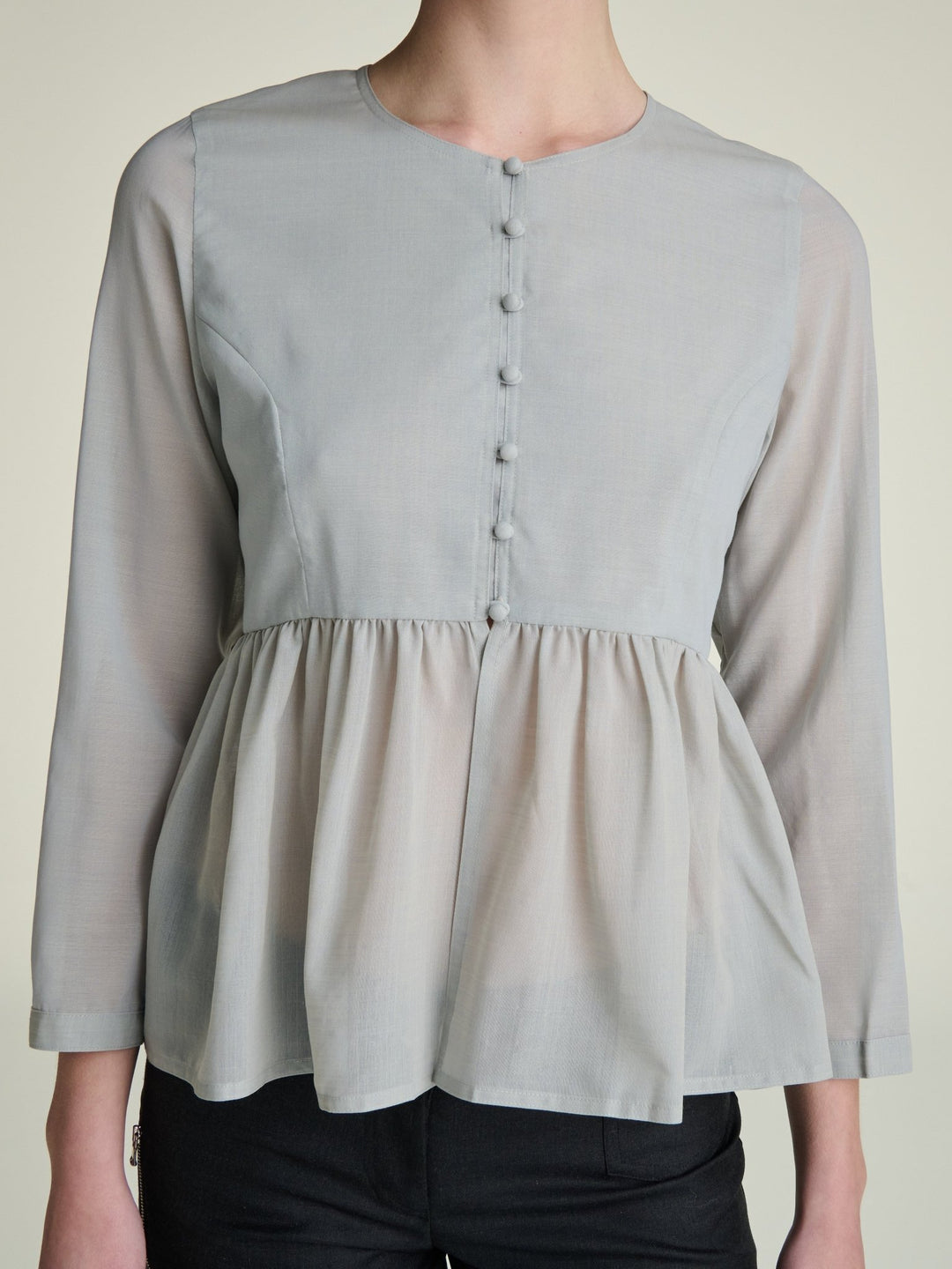Light gray blouse with a peplum waist abd fabric covered buttons on a neutral background