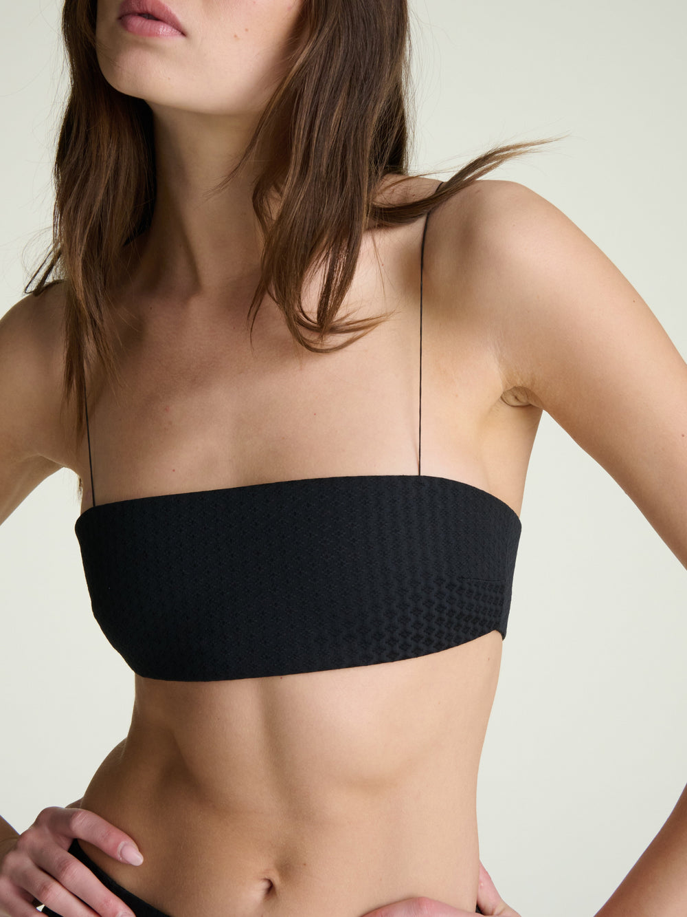 torso view of woman wearing a black bandeau with thin micro elastic straps on a grey background