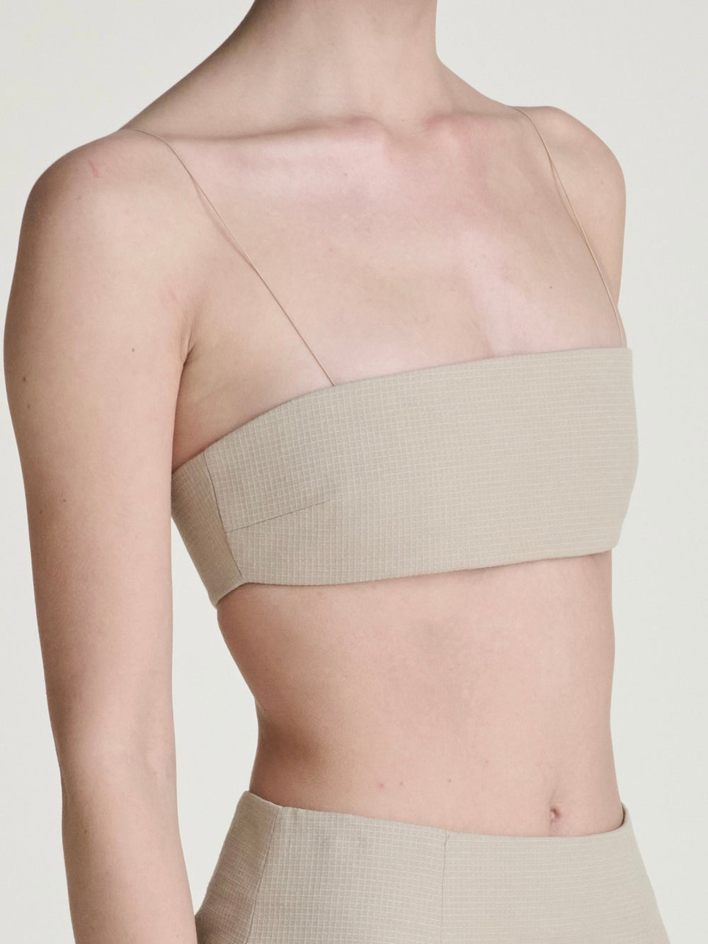 the bust neck and waist of a women wearing a khaki bandeau with thin straps and a khaki skirt in the same fabric on a grey background