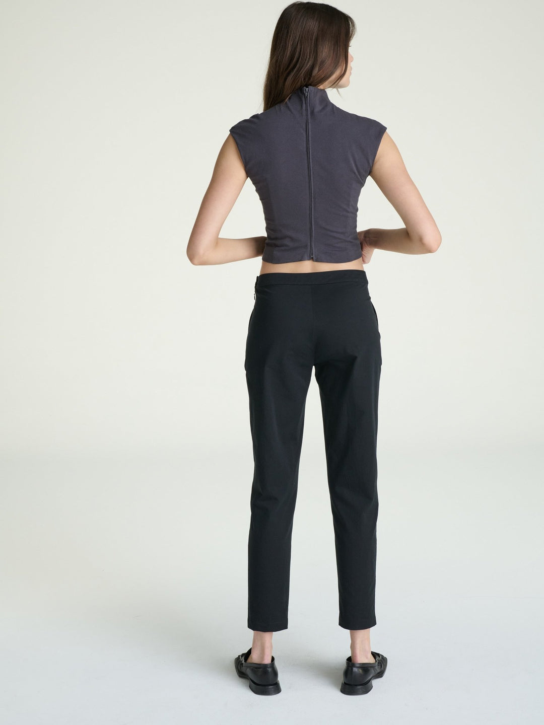 Person wearing a dark gray sleeveless top and black pants on a white background