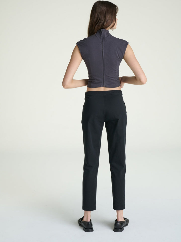 Person wearing a dark gray sleeveless top and black pants on a white background
