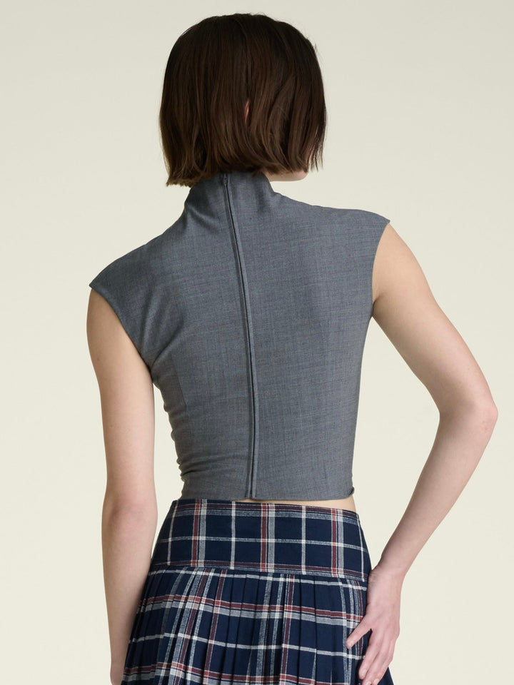 model wearing a light heather grey sleeveless mock-neck top and a navy and red plaid pleated skirt, shown from the back