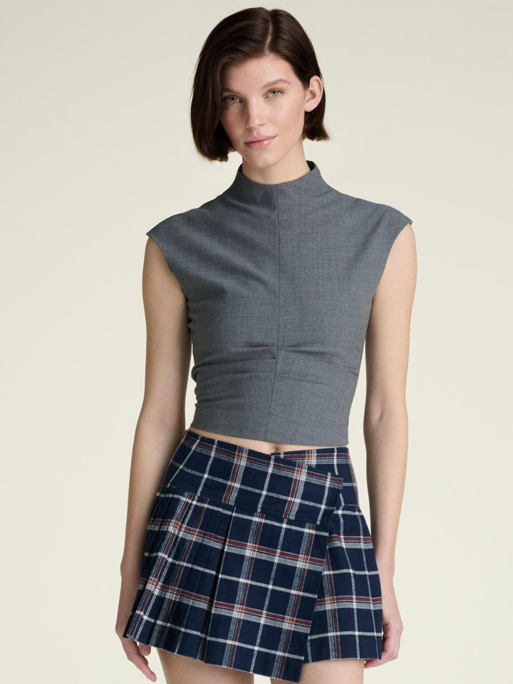 A woman wearing a grey mockneck sleeveless top paired with a plaid skirt.