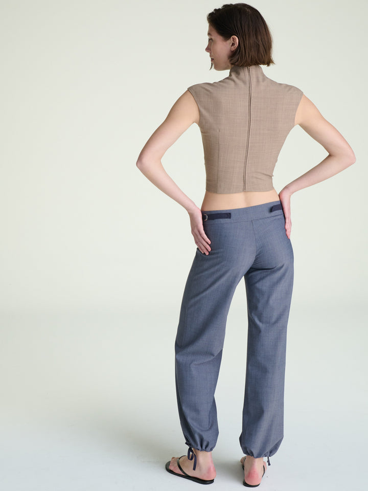 Person wearing a beige sleeveless top and gray pants on a light background