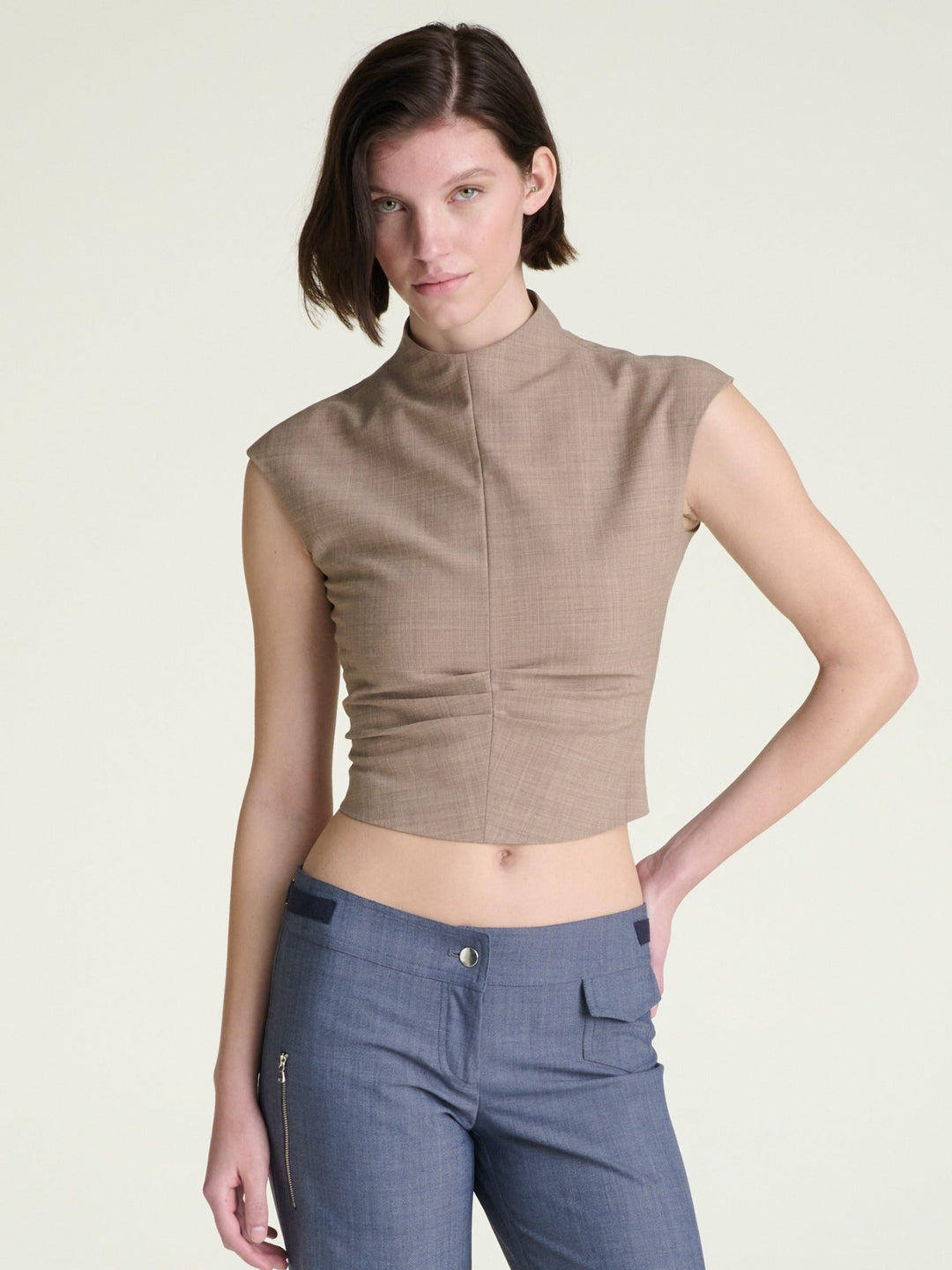 Woman wearing a light brown sleeveless top and blue pants on a light background