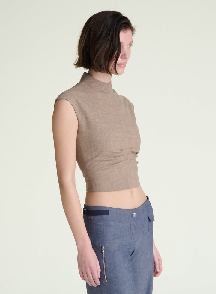 Woman wearing a brown sleeveless top and blue pants on a light background