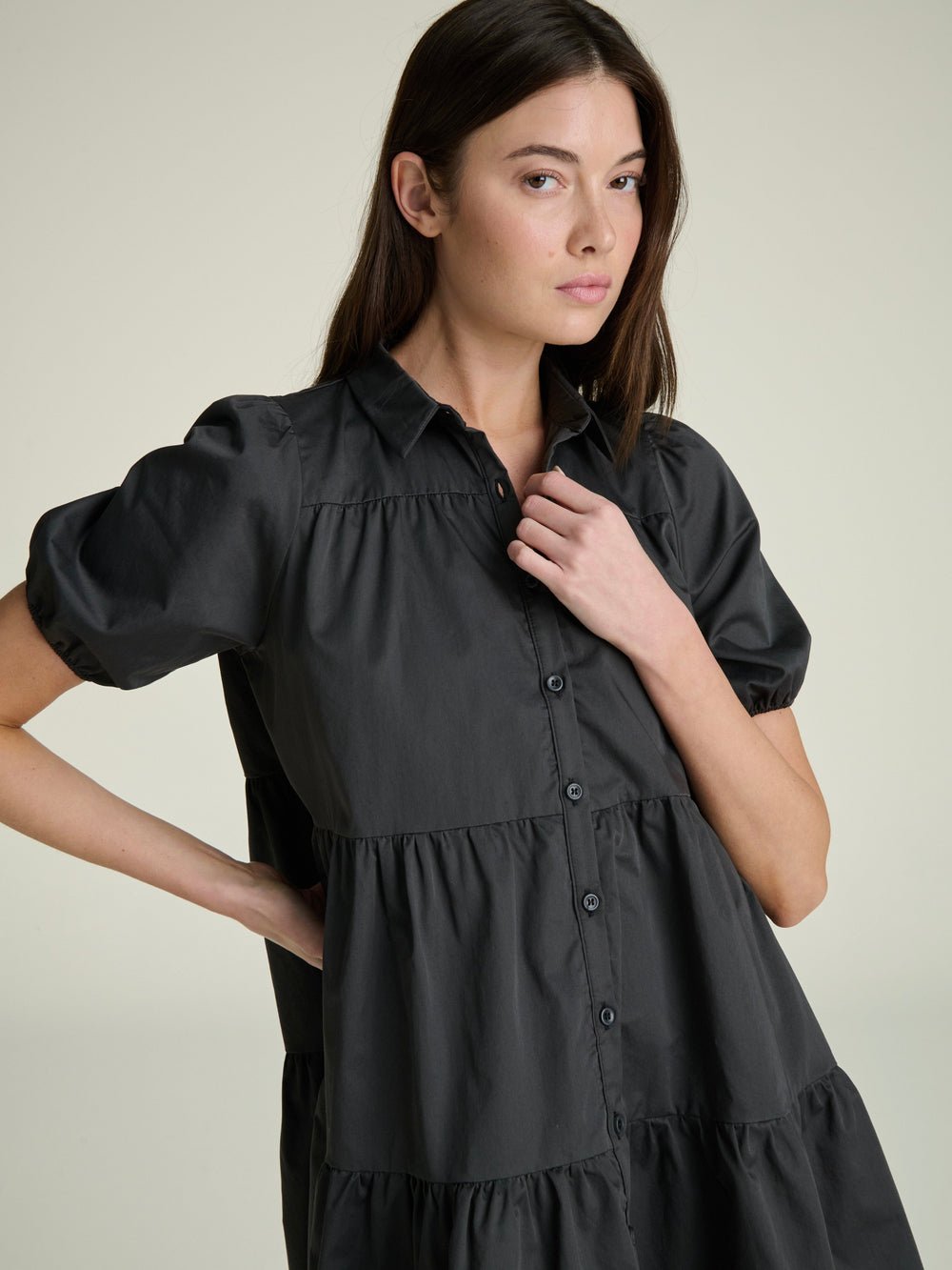 A woman wearing a slate gray A-line shirt dress with a full button-down front and short sleeves on a grey background