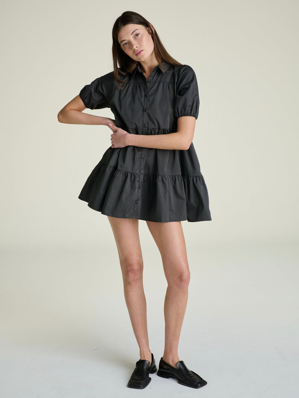 woman wearing a slate-grey a-line  mini dress with a full button down panel and short puff sleeves on a grey background