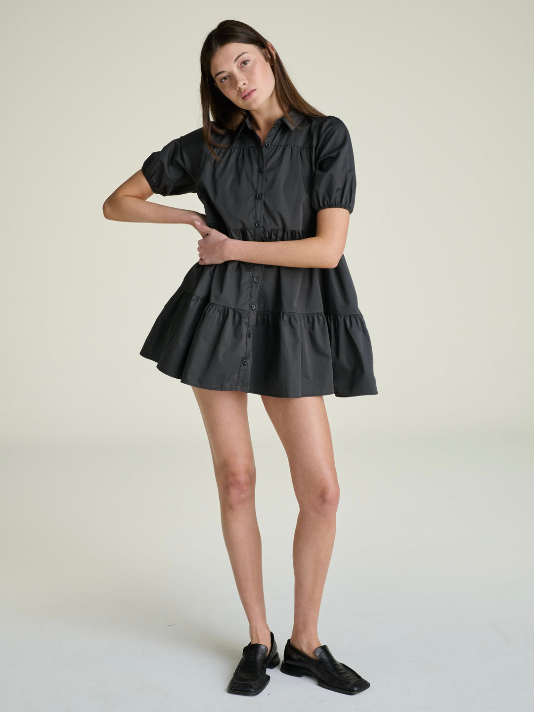 woman wearing a slate-grey a-line  mini dress with a full button down panel and short puff sleeves on a grey background