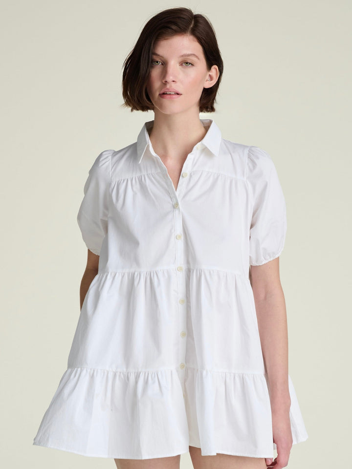 A woman wearing a white A-line shirt dress with a full button-down front and a collar.