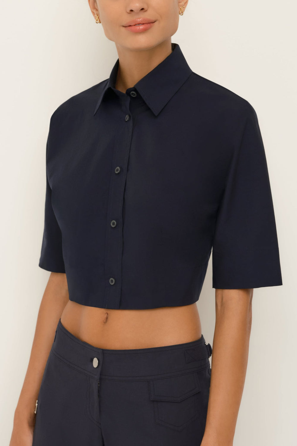 Person wearing a navy blue cropped shirt with short sleeves on a white background
