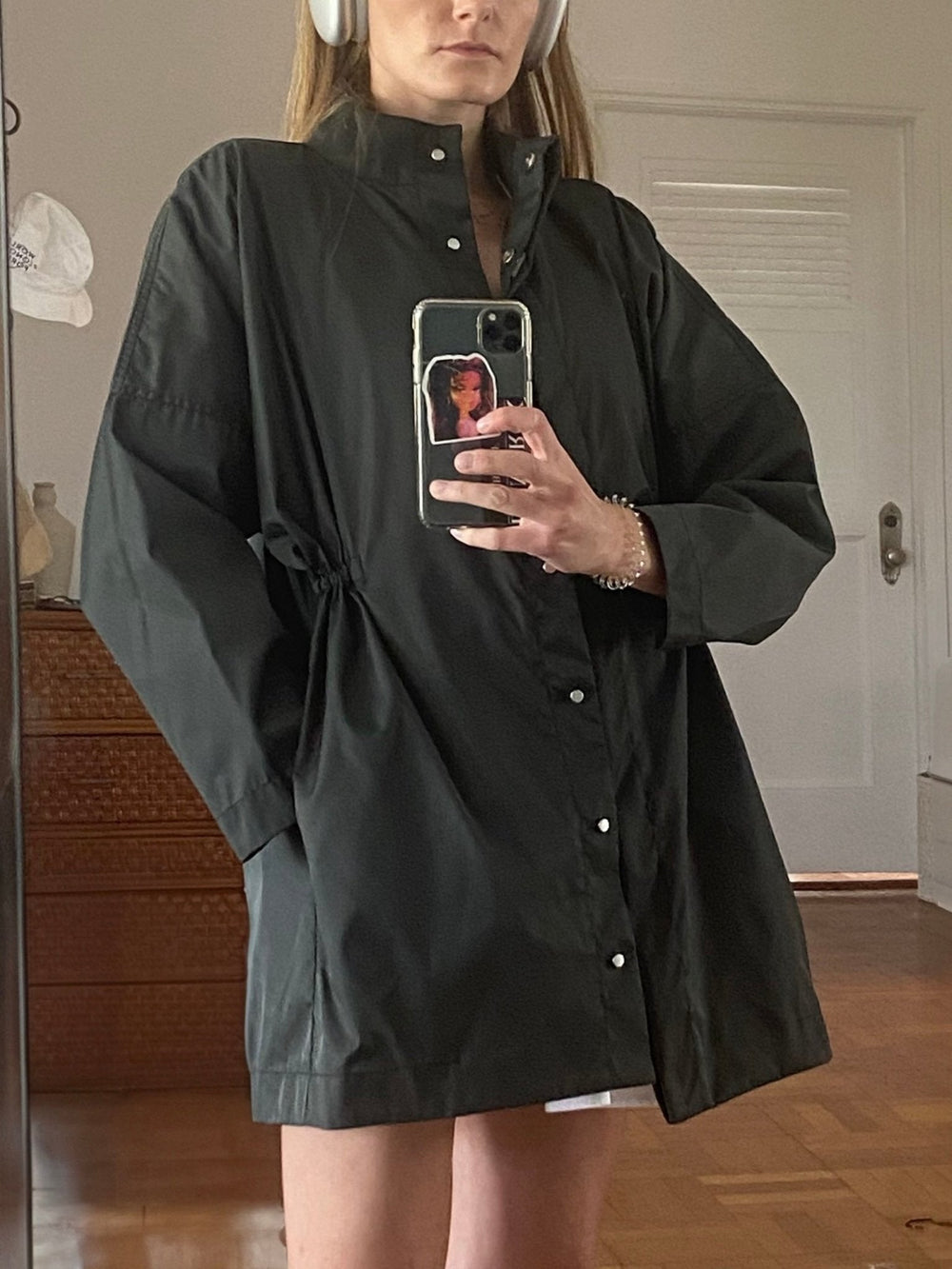 Selfie of a model in a mirror wearing an oversized dark grey jacket with a button-down front and wide sleeves.