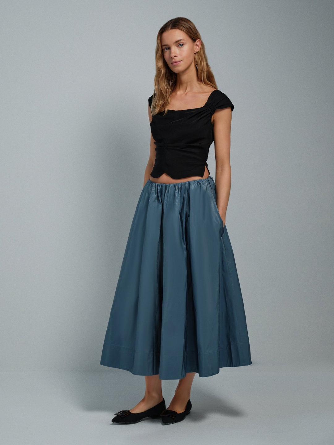 Woman wearing a black viscose corset top and blue taffeta skirt on a gray background