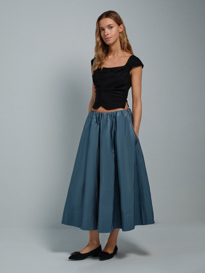 Woman wearing a black viscose corset top and blue taffeta skirt on a gray background