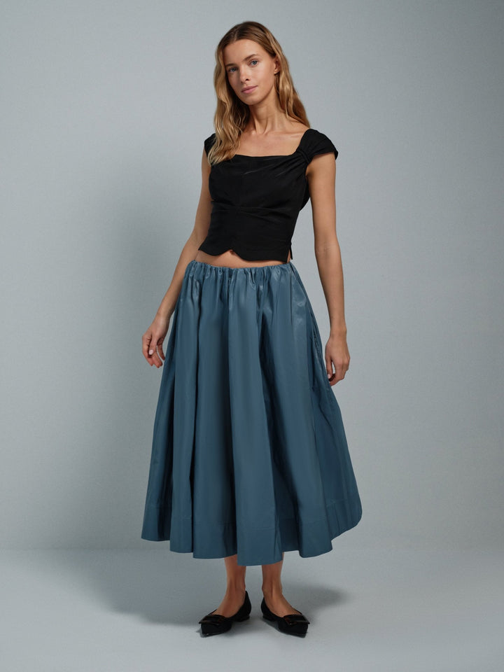 Woman wearing a black top and blue skirt on a gray background