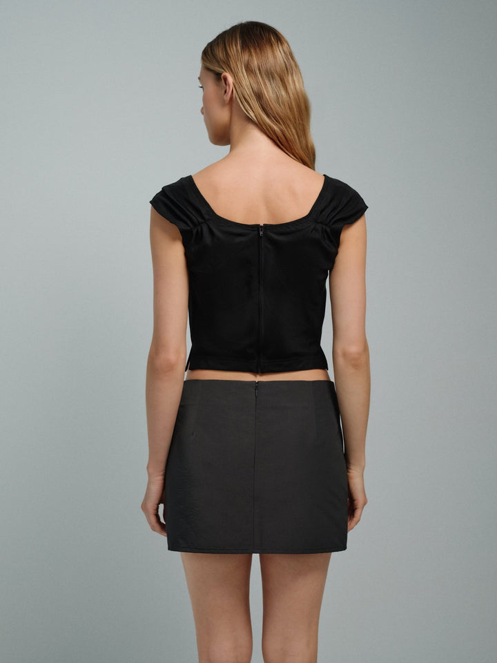 Woman wearing a black sleeveless corset top with a hidden back zipper. She also wears a dark grey mini skirt