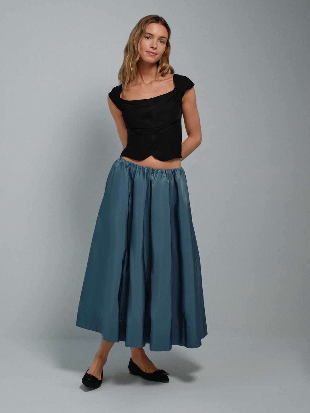 Woman wearing a black viscose corset top and blue taffeta skirt against a gray background