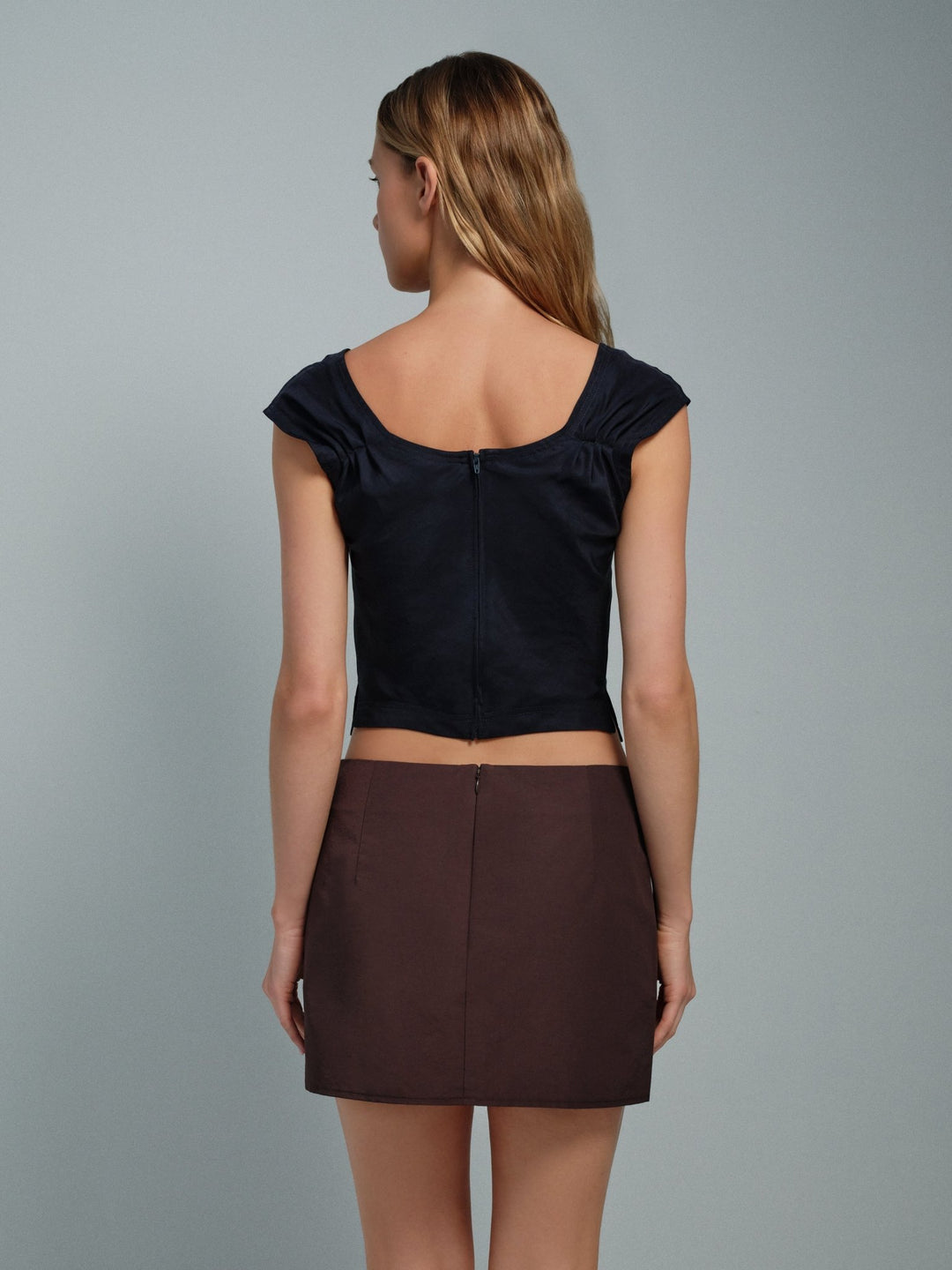 Woman wearing a midnight navy blue top and brown skirt on a gray background