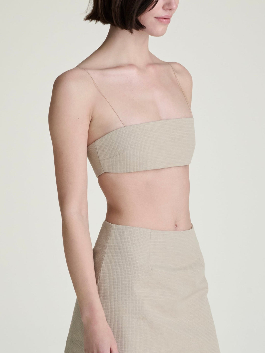 Woman wearing a beige bandeau top and skirt set on a plain grey background