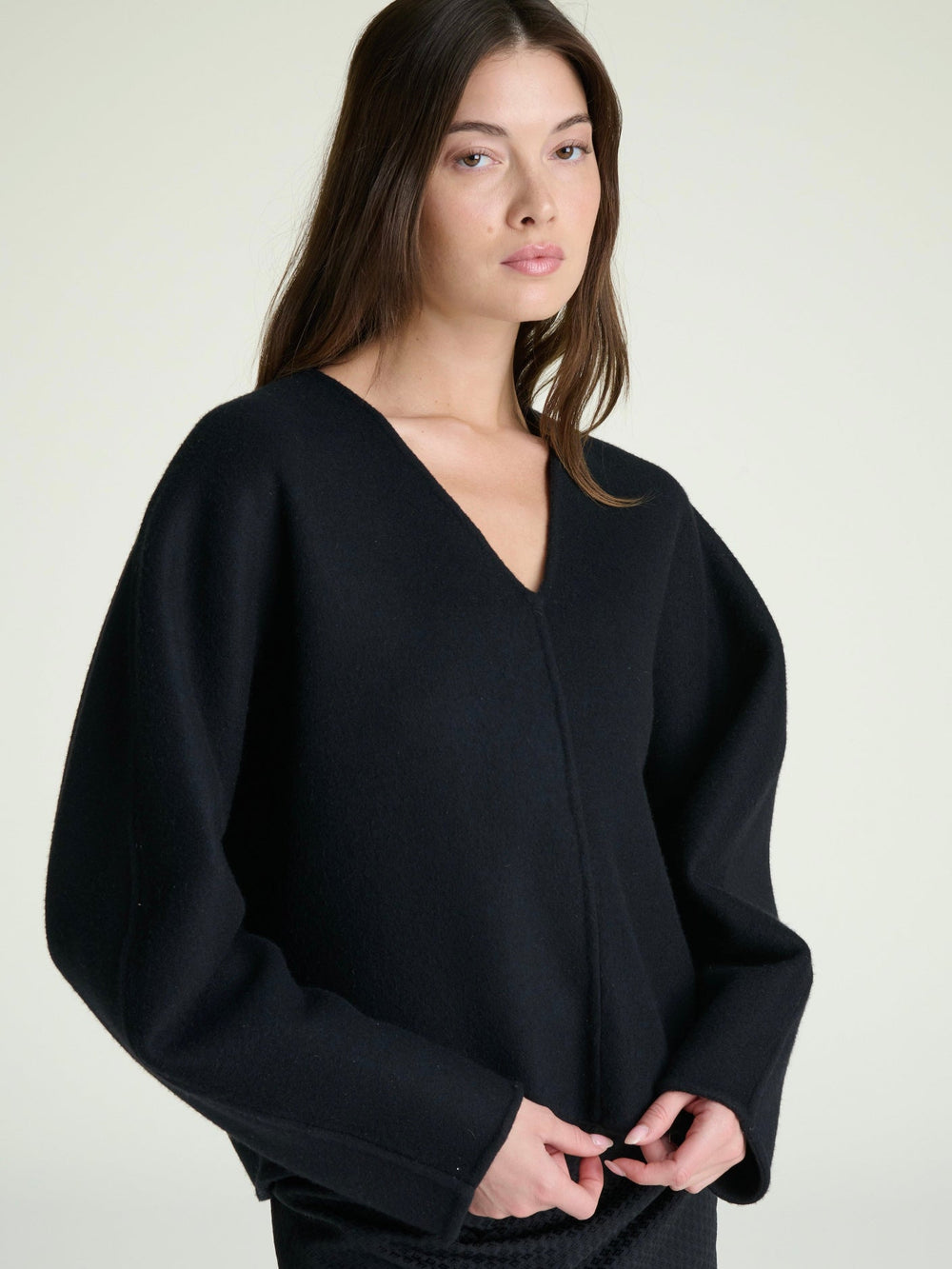 woman wearing a v-neck black sweater in heavy weight wool on a grey background