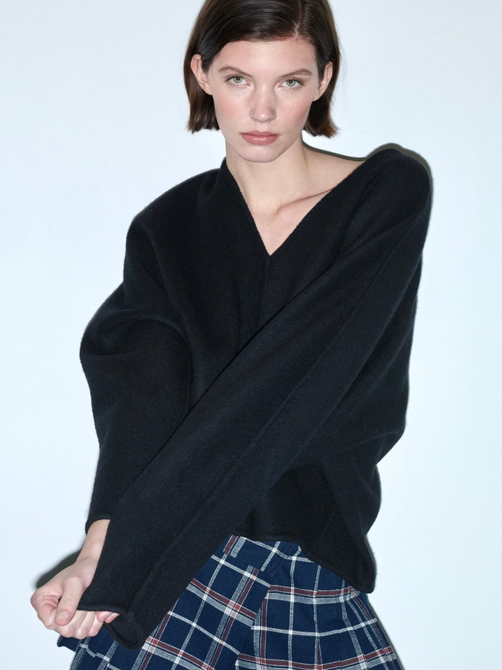 Woman wearing a black sweater over a plaid skirt on a gray background