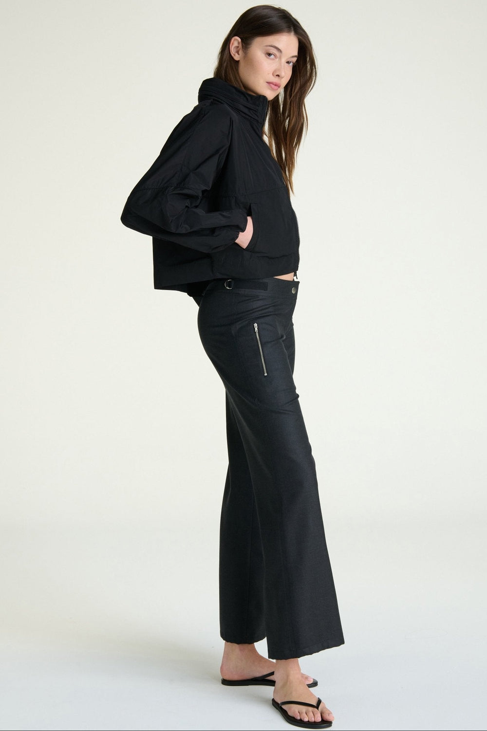 Woman wearing a black outfit with a high collar and flared pants on a white background