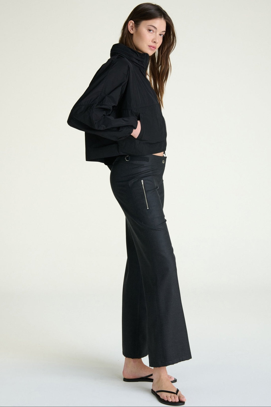 Woman wearing a black outfit with a high collar and flared pants on a white background