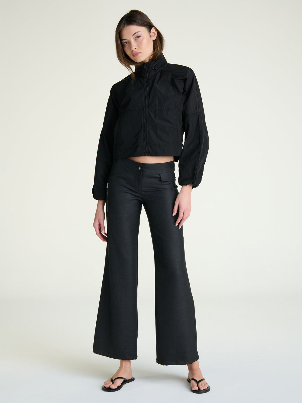 Person wearing a black windbreaker jacket and pants on a gray background