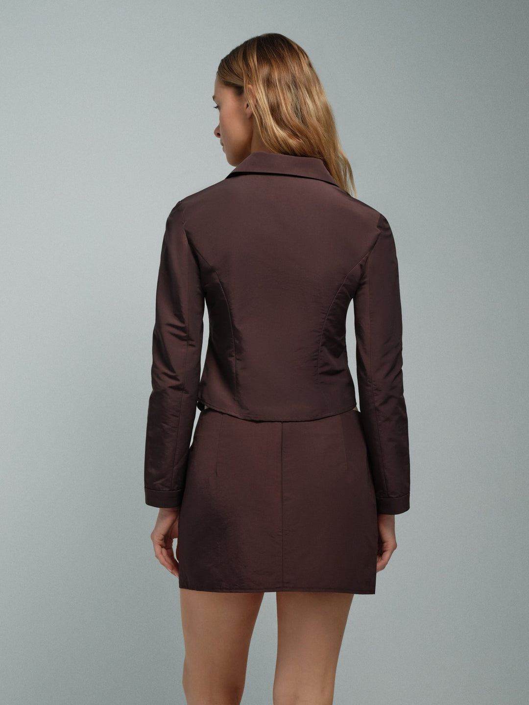 Model wearing the brown Slim Zip Jacket, a tailored jacket made of faille with princess seams and a curved hem. 