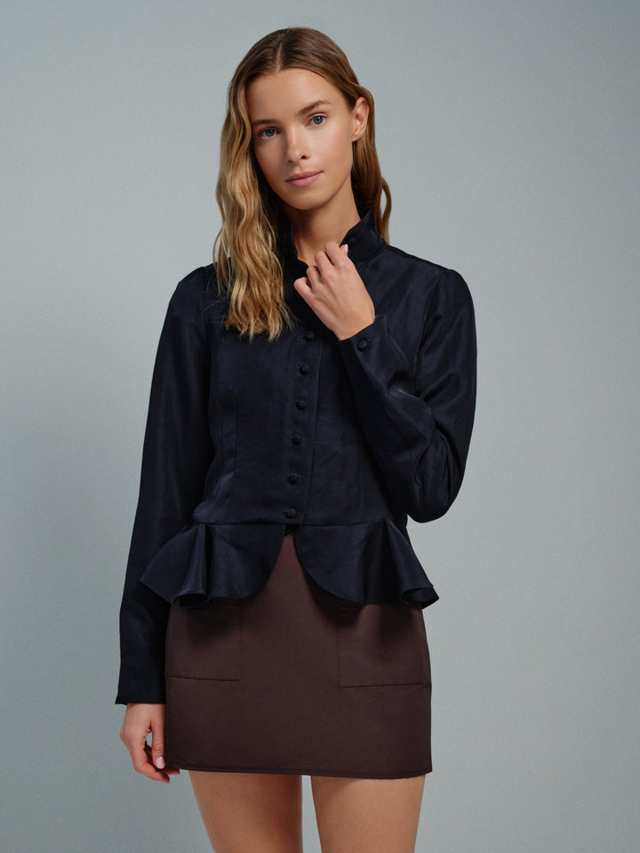 Woman wearing a dark blue jacket blouse with ruffled details on a gray background