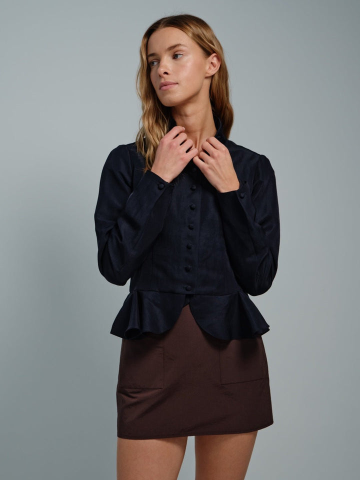 Woman wearing a dark blue peplum top and brown skirt against a gray background