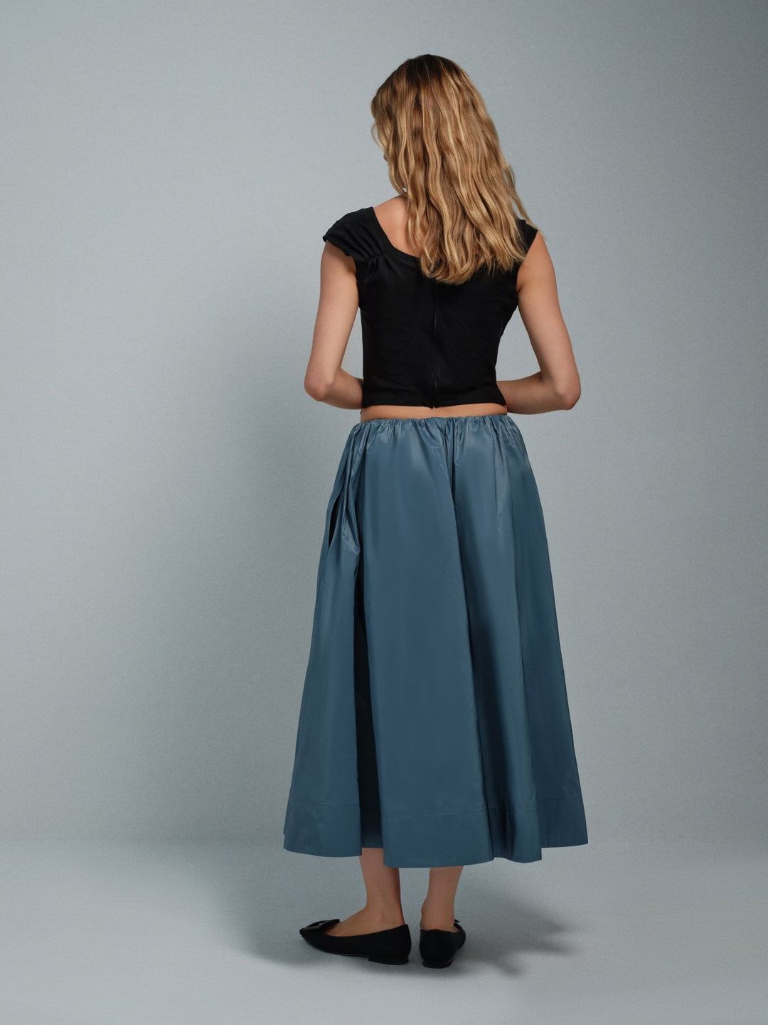 Woman wearing a black top and blue skirt against a gray background