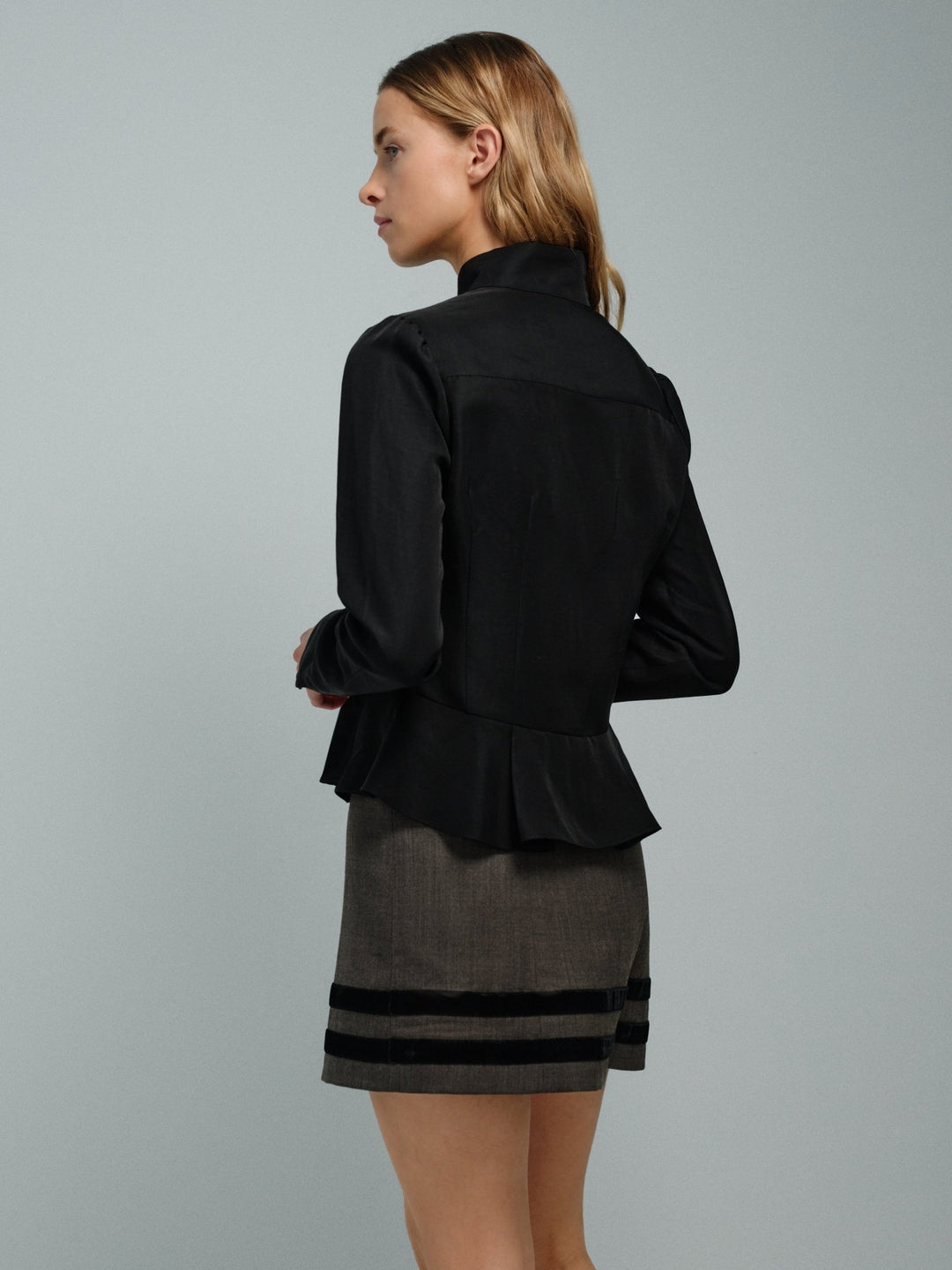 Woman wearing a black peplum jacket and gray skirt with black stripes on a gray background