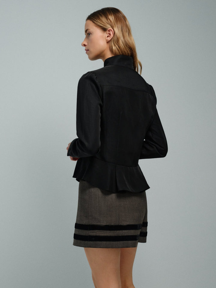 Woman wearing a black peplum jacket and gray skirt with black stripes on a gray background