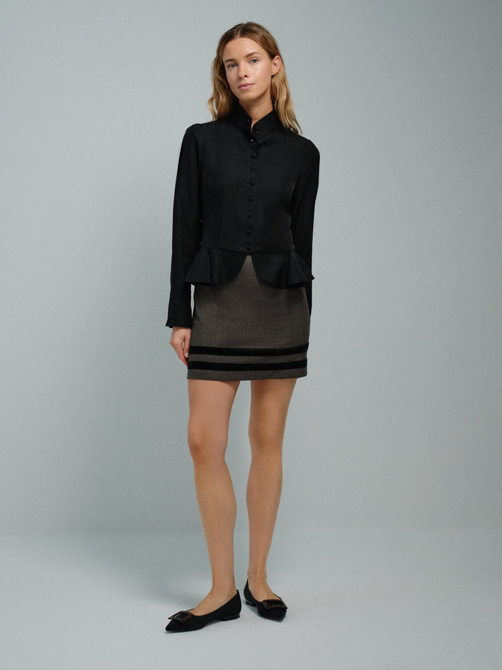 Woman wearing a black jacket and gray skirt with black accents on a gray background