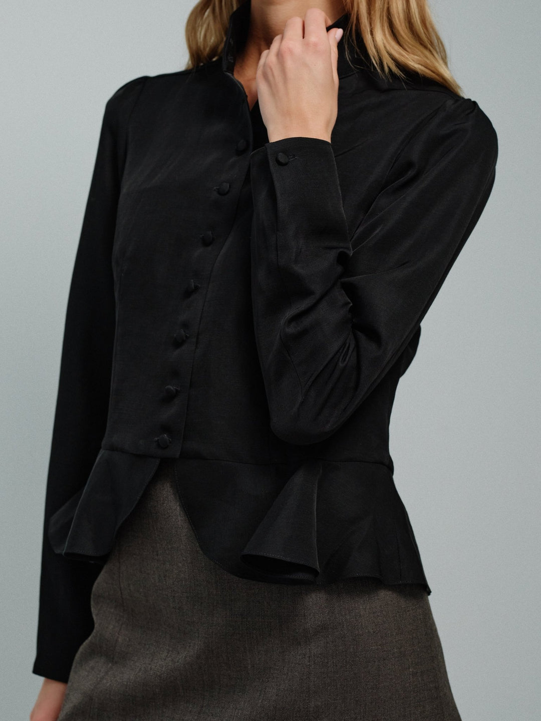 Black jacket blouse with ruffled details worn by a woman on a gray background