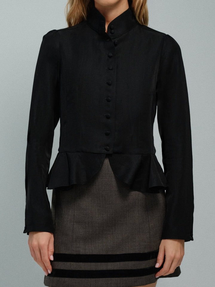 Woman wearing a black high collar jacket with a peplum waist over a gray dress on a gray background